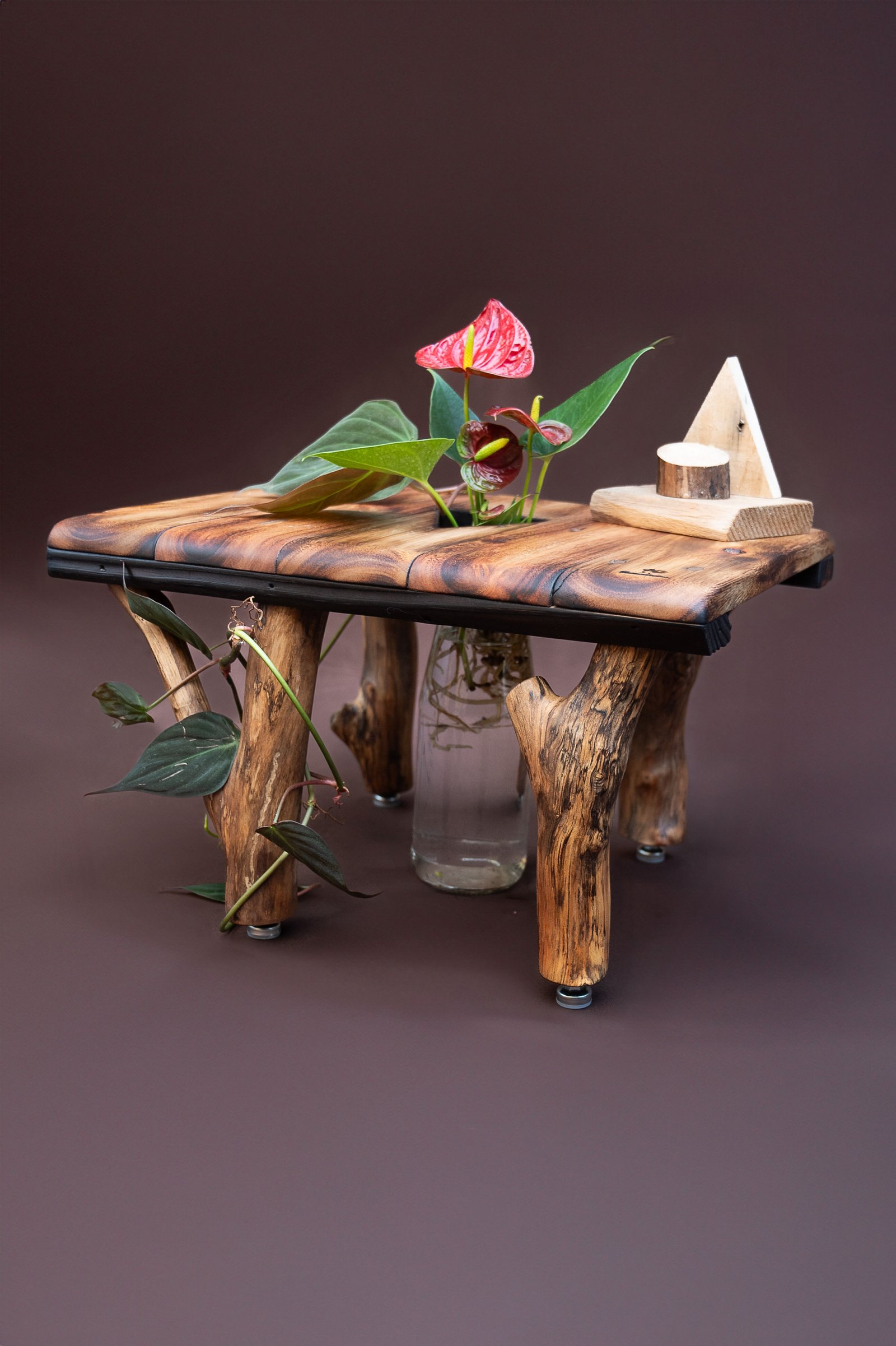Mesa artesanal de madeira com flores vermelhas e um vaso de vidro entre os pés